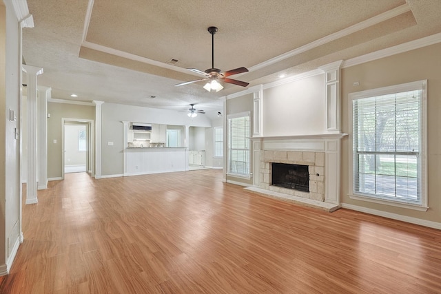 unfurnished living room featuring ceiling fan, ornamental molding, a textured ceiling, light hardwood / wood-style flooring, and a tray ceiling