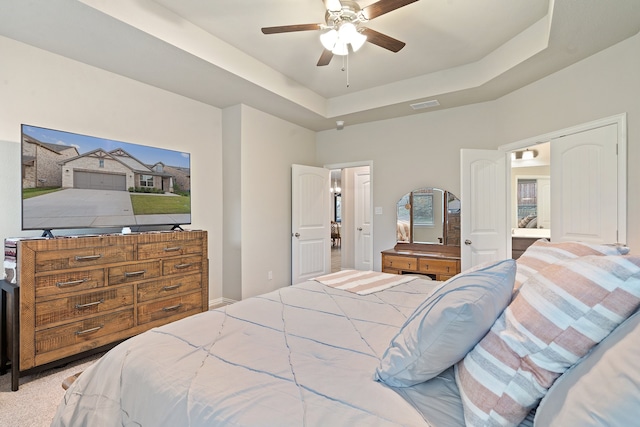 bedroom with ensuite bath, a raised ceiling, light colored carpet, and ceiling fan