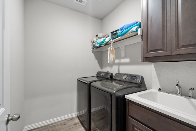 laundry room featuring sink, light hardwood / wood-style flooring, washing machine and dryer, and cabinets