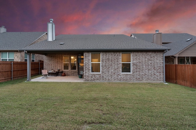 back house at dusk with a patio area and a yard