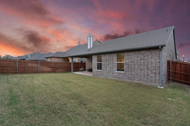 back house at dusk with a patio area and a lawn