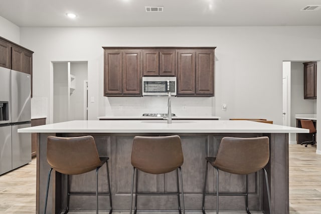 kitchen with a kitchen island with sink, stainless steel appliances, and light wood-type flooring