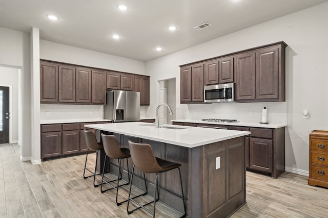 kitchen with light hardwood / wood-style floors, appliances with stainless steel finishes, sink, and an island with sink