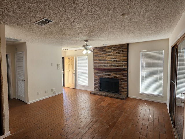 unfurnished living room featuring a textured ceiling, ceiling fan, dark hardwood / wood-style floors, and a brick fireplace