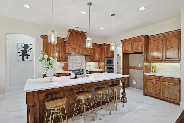 kitchen featuring decorative light fixtures, backsplash, stainless steel appliances, and a center island with sink