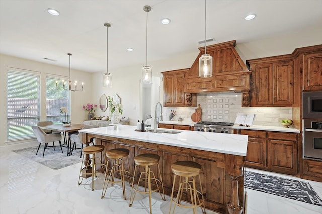 kitchen featuring appliances with stainless steel finishes, sink, an inviting chandelier, hanging light fixtures, and an island with sink