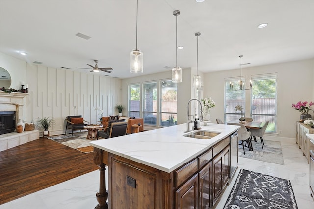 kitchen featuring light stone countertops, sink, pendant lighting, a kitchen island with sink, and ceiling fan with notable chandelier