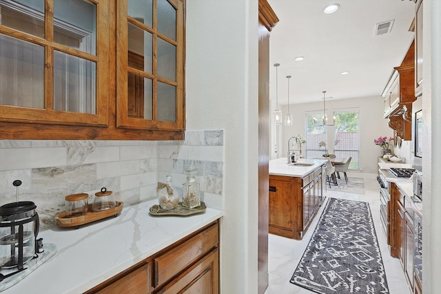 kitchen with sink, light stone counters, backsplash, a chandelier, and decorative light fixtures