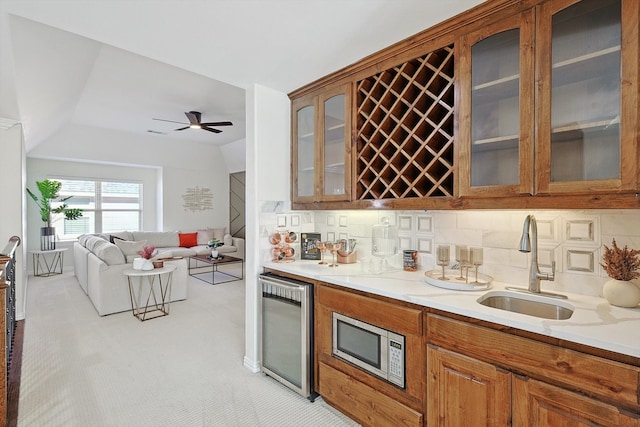 kitchen featuring stainless steel microwave, sink, wine cooler, tasteful backsplash, and light colored carpet