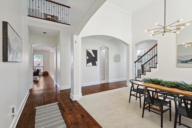 foyer featuring dark hardwood / wood-style flooring, a towering ceiling, ornamental molding, and an inviting chandelier