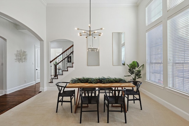 carpeted dining room featuring ornamental molding, a towering ceiling, and an inviting chandelier