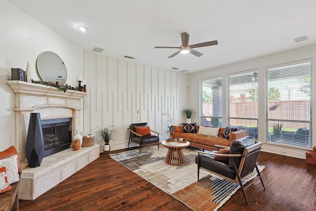 living room with a premium fireplace, ceiling fan, and dark wood-type flooring