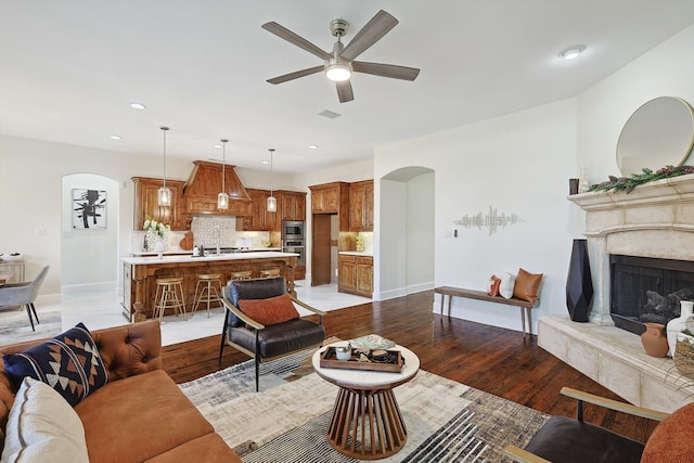 living room with a high end fireplace, light wood-type flooring, and ceiling fan