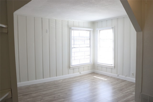 unfurnished room with light wood-type flooring and a textured ceiling