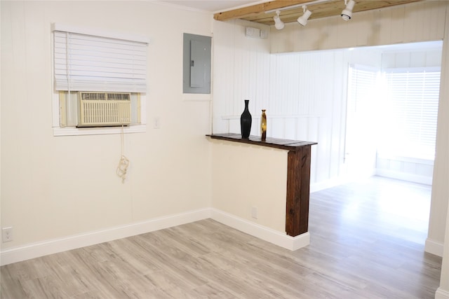 empty room featuring cooling unit, beamed ceiling, electric panel, bar area, and light wood-type flooring