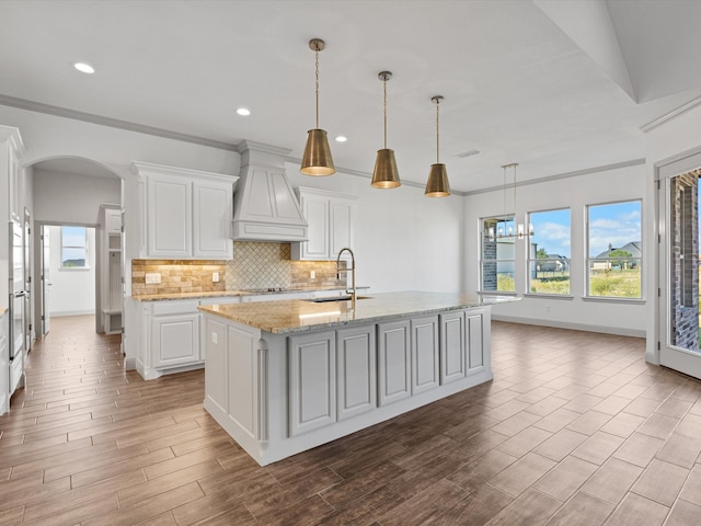 kitchen featuring white cabinetry, hanging light fixtures, hardwood / wood-style flooring, and an island with sink