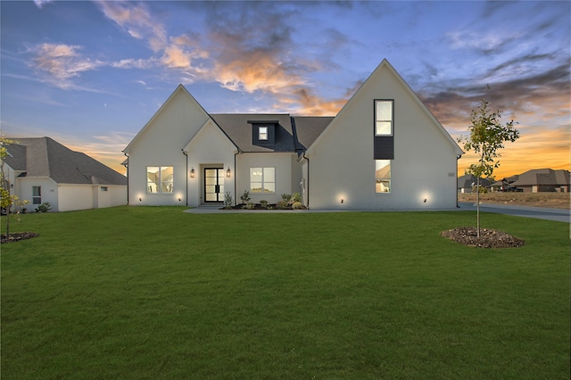 back house at dusk featuring a lawn