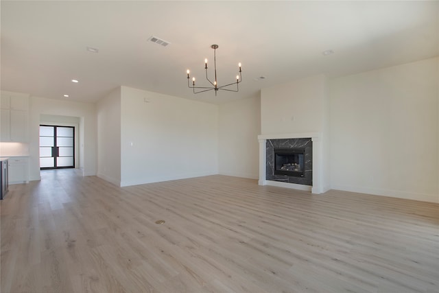 unfurnished living room featuring a high end fireplace, a chandelier, and light hardwood / wood-style flooring