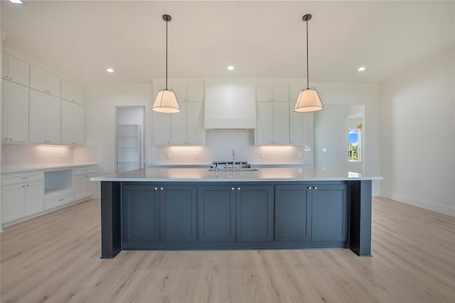 kitchen with light wood-type flooring, white cabinets, custom range hood, hanging light fixtures, and a spacious island