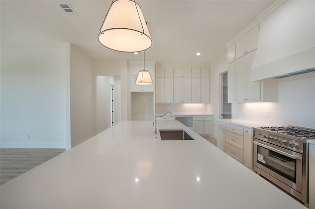 kitchen with white cabinets, stainless steel stove, premium range hood, sink, and decorative light fixtures