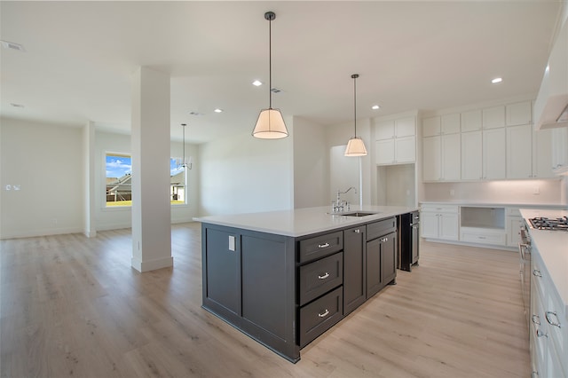 kitchen featuring white cabinets, hanging light fixtures, sink, a kitchen island with sink, and light hardwood / wood-style flooring