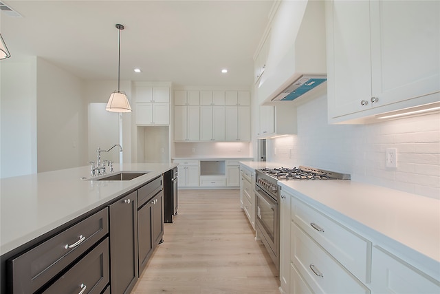 kitchen featuring white cabinets, sink, decorative light fixtures, high end stainless steel range oven, and custom range hood