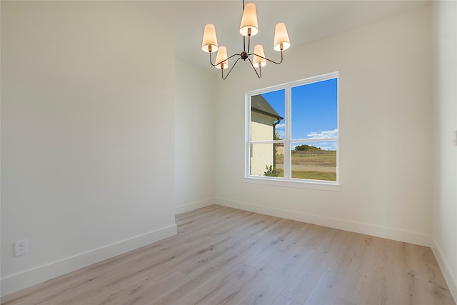 spare room featuring a chandelier and light hardwood / wood-style flooring