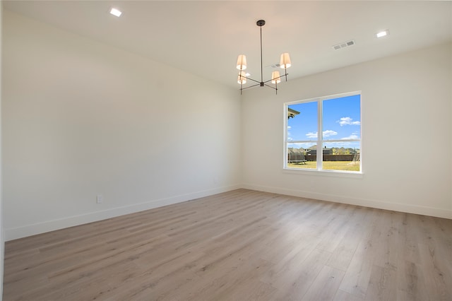 spare room featuring an inviting chandelier and light hardwood / wood-style flooring