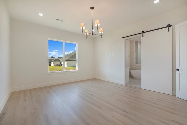 empty room featuring a notable chandelier, light wood-type flooring, and a barn door