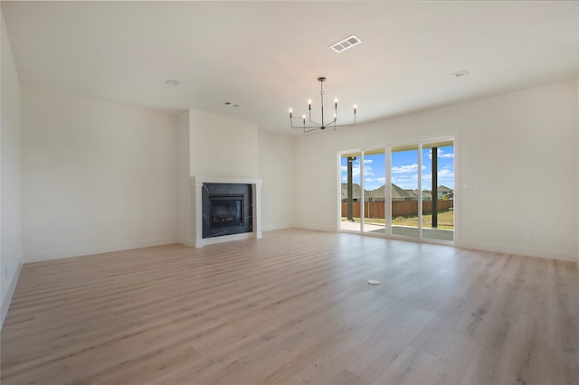 unfurnished living room featuring an inviting chandelier, a premium fireplace, and light hardwood / wood-style floors