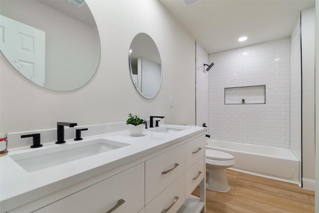 full bathroom featuring vanity, hardwood / wood-style flooring, tiled shower / bath combo, and toilet