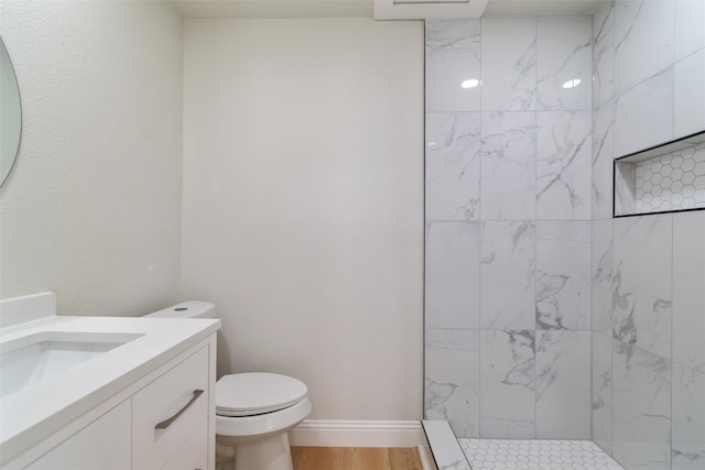 bathroom featuring hardwood / wood-style flooring, a tile shower, vanity, and toilet