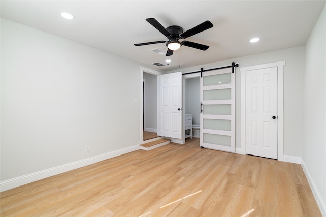 unfurnished bedroom featuring ceiling fan, a barn door, and light hardwood / wood-style floors