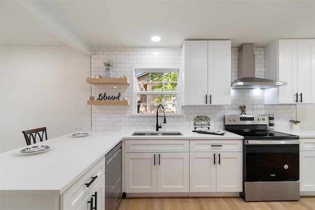 kitchen featuring wall chimney range hood, light wood-type flooring, sink, white cabinets, and appliances with stainless steel finishes