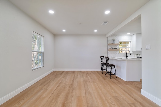 interior space featuring light hardwood / wood-style floors, white cabinets, a breakfast bar, and a healthy amount of sunlight