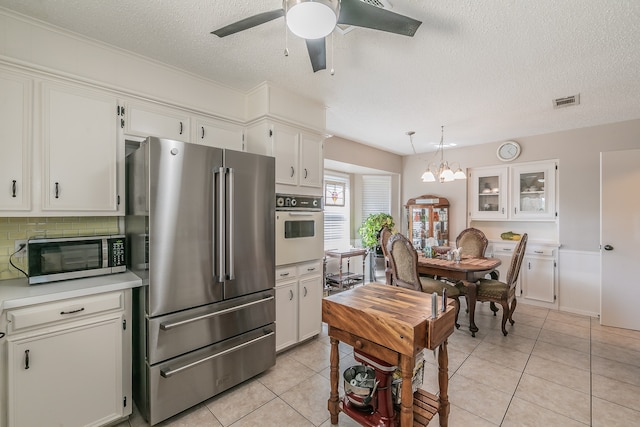 kitchen with tasteful backsplash, ceiling fan with notable chandelier, white cabinets, appliances with stainless steel finishes, and light tile patterned floors