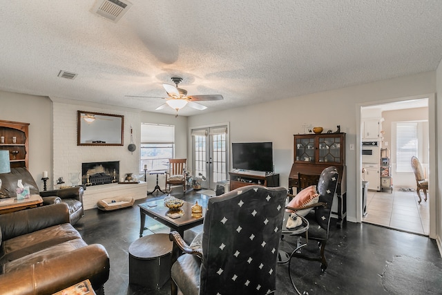 living room featuring ceiling fan, dark tile patterned flooring, a brick fireplace, french doors, and a textured ceiling