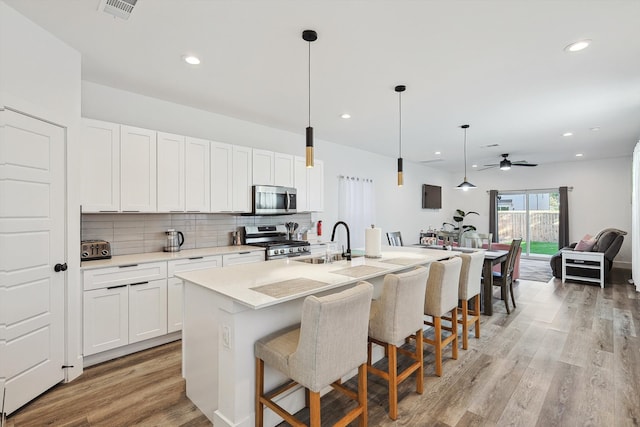 kitchen with appliances with stainless steel finishes, white cabinets, decorative light fixtures, and a center island with sink