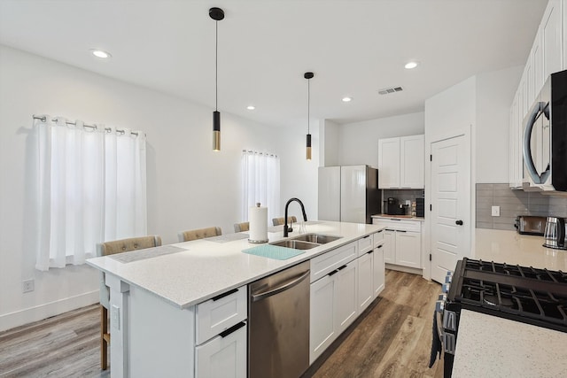 kitchen featuring appliances with stainless steel finishes, white cabinetry, hardwood / wood-style flooring, a breakfast bar, and a kitchen island with sink