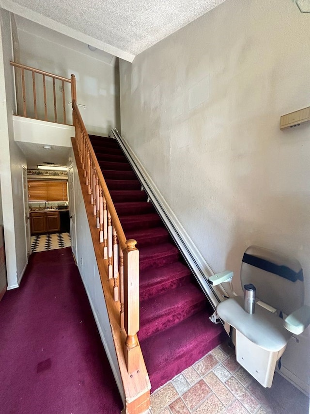 stairs with carpet flooring, sink, and a textured ceiling