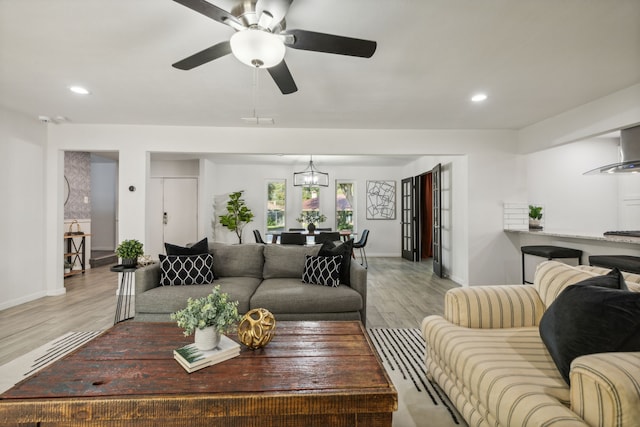 living room featuring ceiling fan with notable chandelier and light wood-type flooring