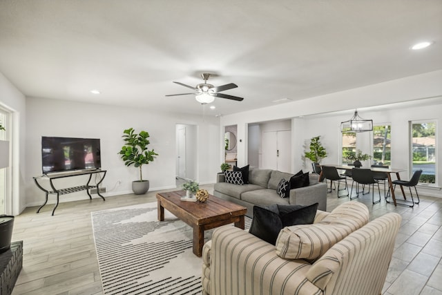 living room featuring ceiling fan with notable chandelier and light hardwood / wood-style flooring