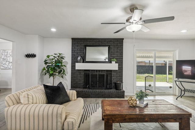 living room with hardwood / wood-style flooring, ceiling fan, and a brick fireplace