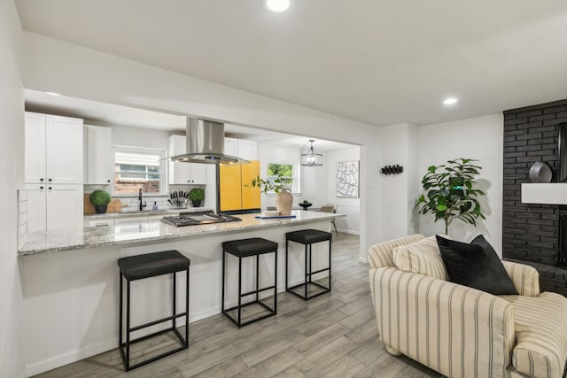 kitchen with white cabinetry, light stone countertops, a kitchen breakfast bar, island range hood, and light wood-type flooring