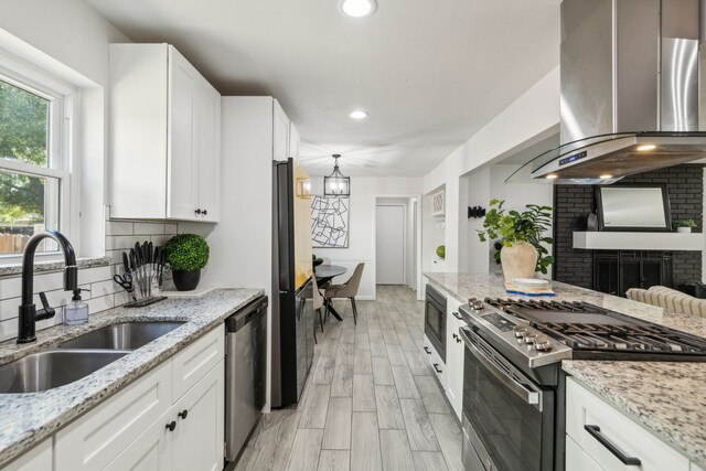 kitchen with white cabinets, wall chimney range hood, sink, appliances with stainless steel finishes, and light stone counters