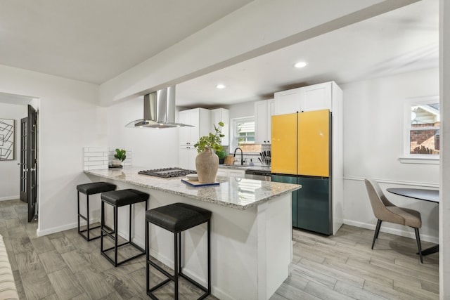 kitchen featuring white cabinetry, wall chimney range hood, kitchen peninsula, a breakfast bar area, and light wood-type flooring