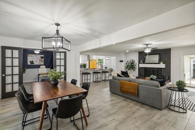 dining room with light hardwood / wood-style floors, ceiling fan with notable chandelier, and a brick fireplace