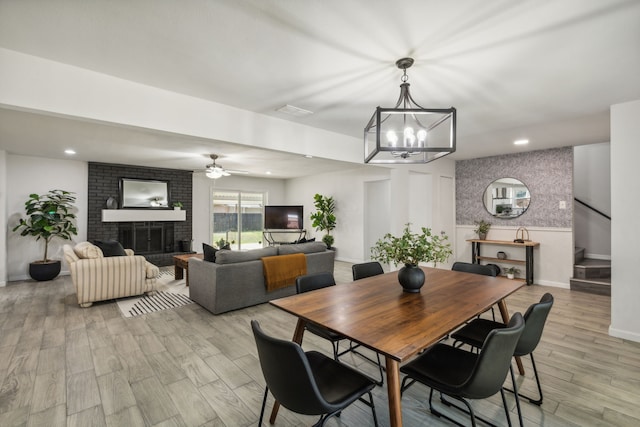 dining room featuring ceiling fan with notable chandelier, light hardwood / wood-style floors, and a fireplace