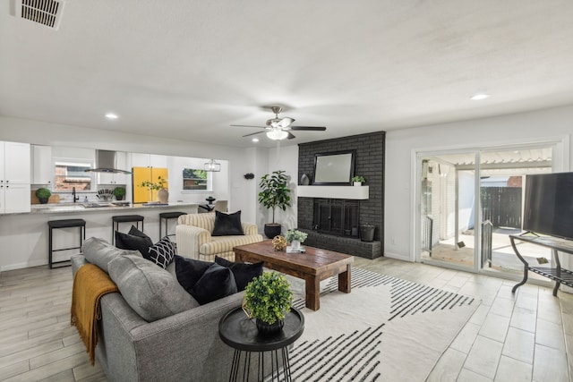 living room with light hardwood / wood-style floors, ceiling fan, a healthy amount of sunlight, and a brick fireplace