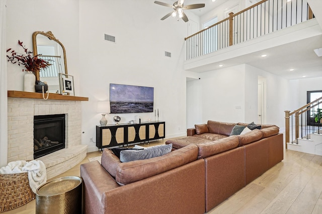 living room featuring a high ceiling, light wood-type flooring, ceiling fan, and a fireplace